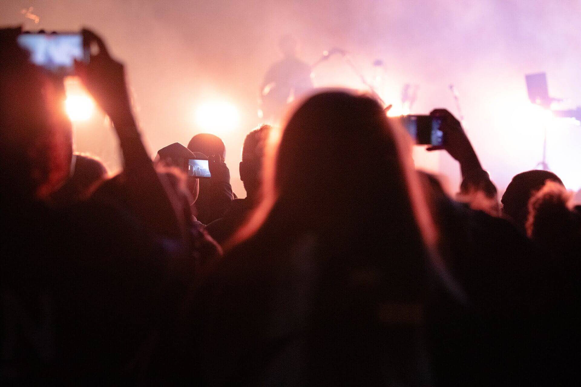 A crowd of people at a concert taking pictures of the band