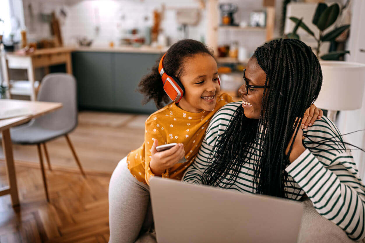 Girl listening music standing by mother working on laptop at home