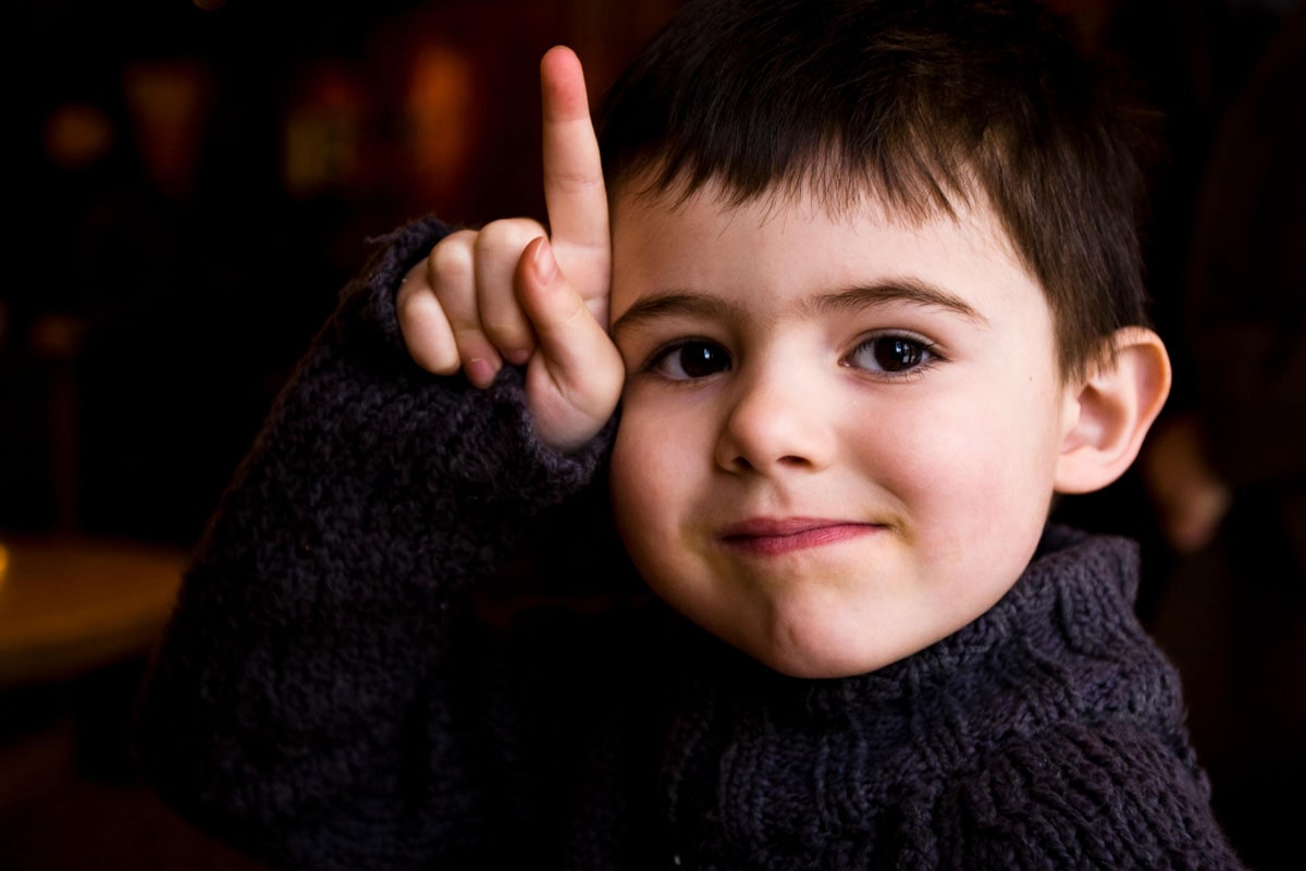 A smiling baby with his hand next to his face and his index finger up