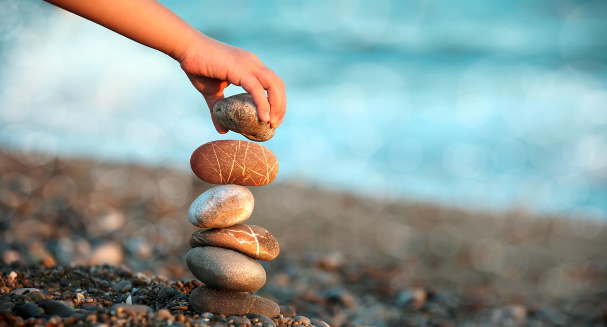 A child's hand building a tower of stones