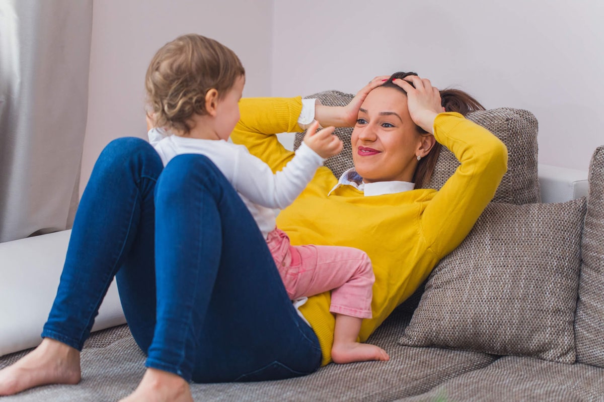 A woman is playing with a baby on the sofa