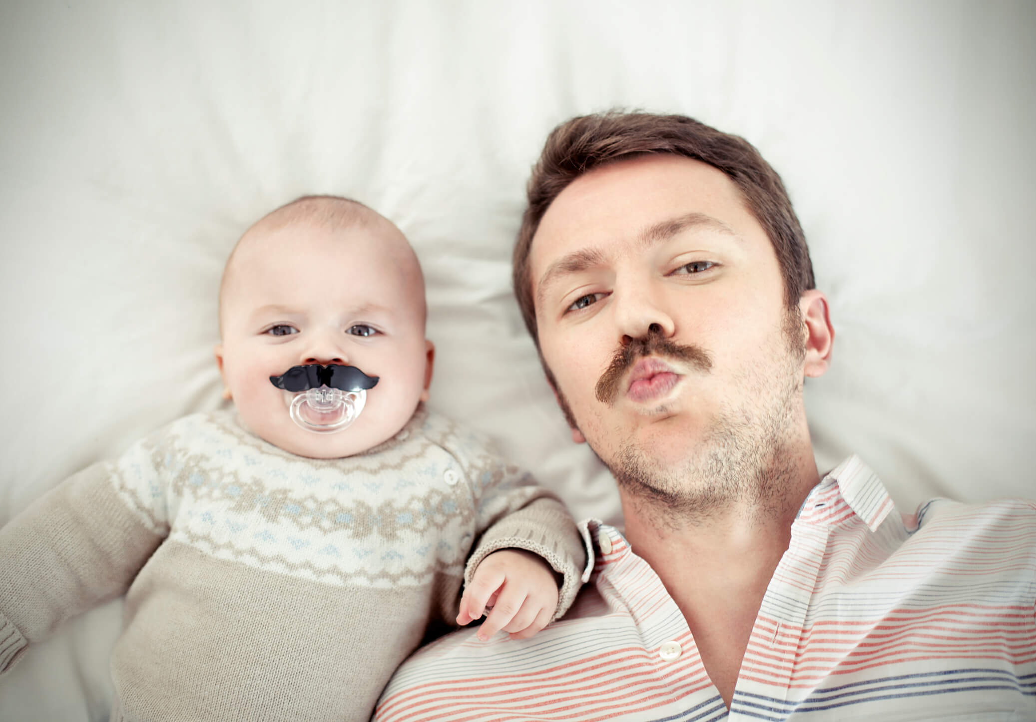 A baby with a mustache pacifier and his dad with a mustache
