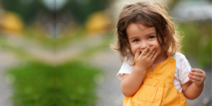 A cute little girl covering her mouth and smiling