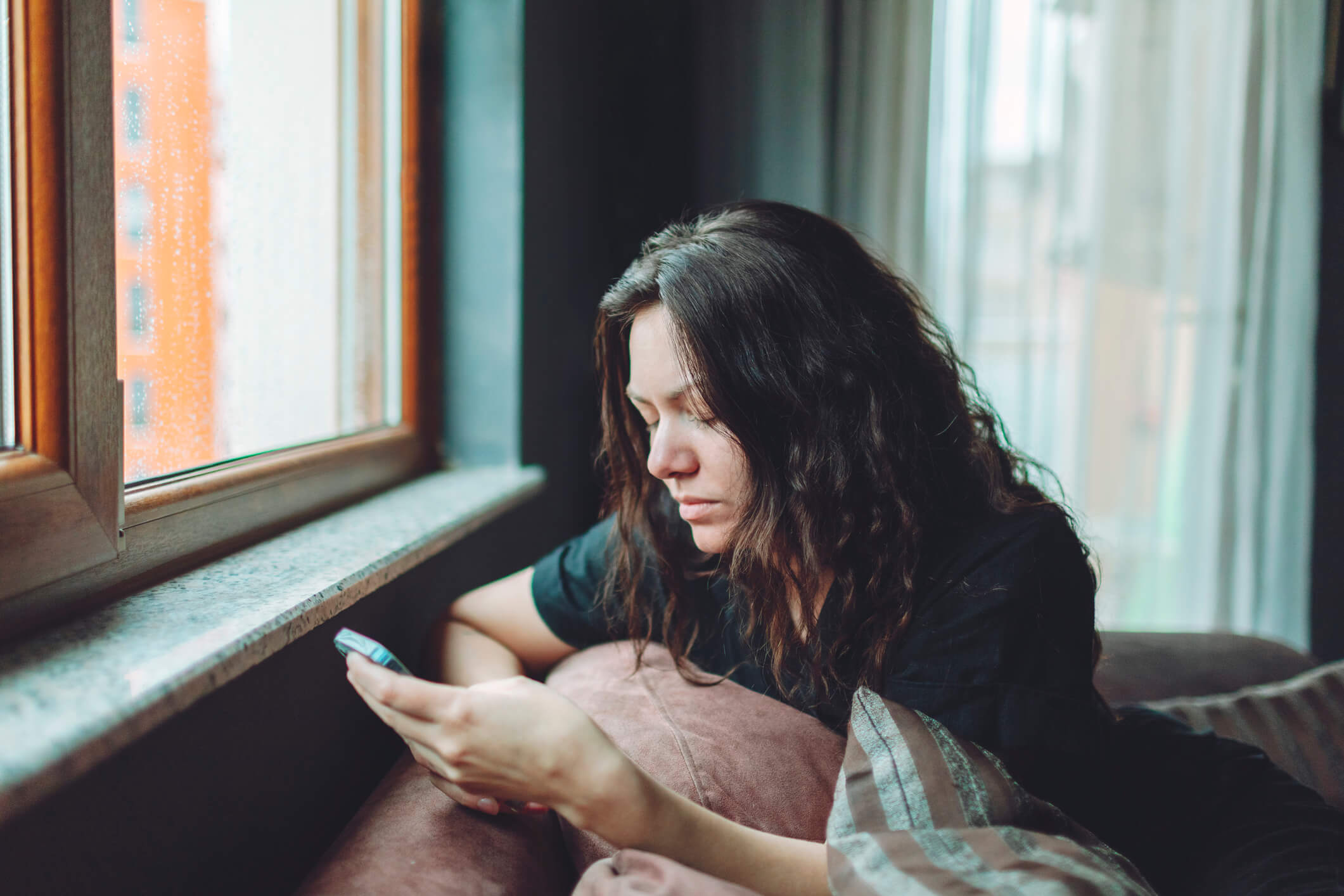 Depressed woman sitting on sofa at home on her phone